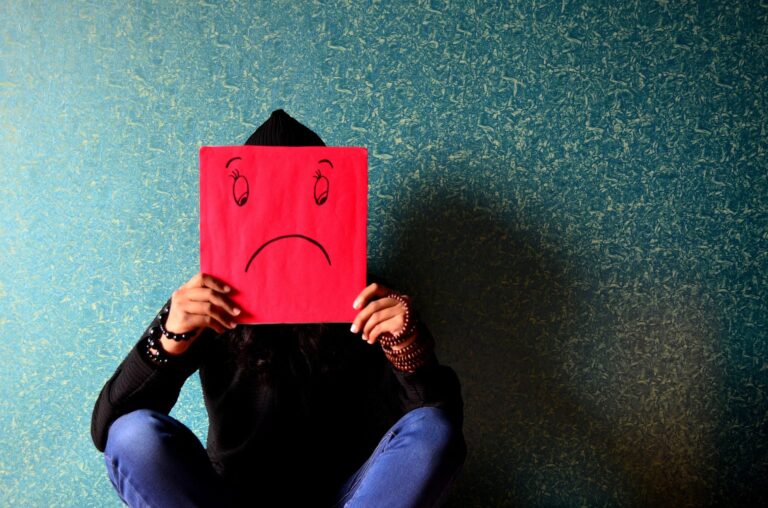 A young person indicates their unhappiness with a sad face drawn on a piece of paper in front of their face