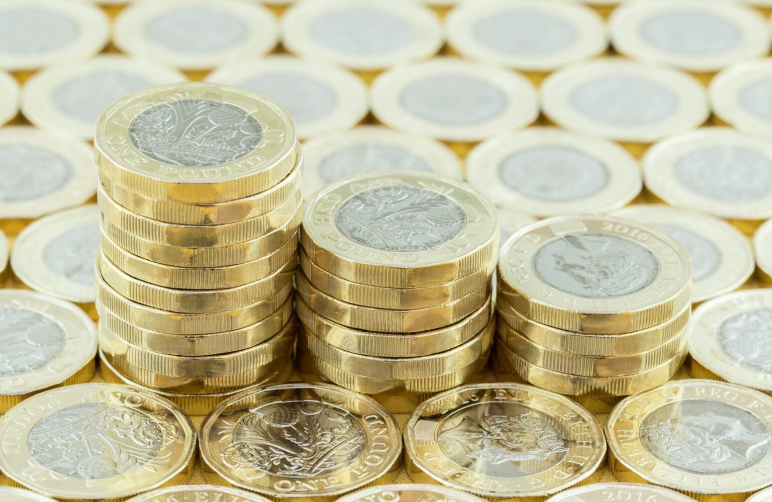 British money, new pound coins in three stacks on a background of more money. New one pound coins introduced in 2017